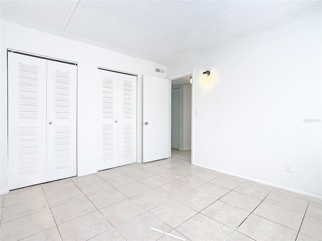 unfurnished bedroom featuring light tile patterned floors, a textured ceiling, and two closets