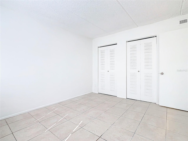 unfurnished bedroom with light tile patterned floors and multiple closets