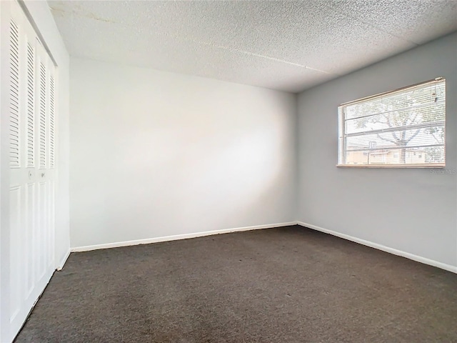 spare room featuring dark carpet and a textured ceiling