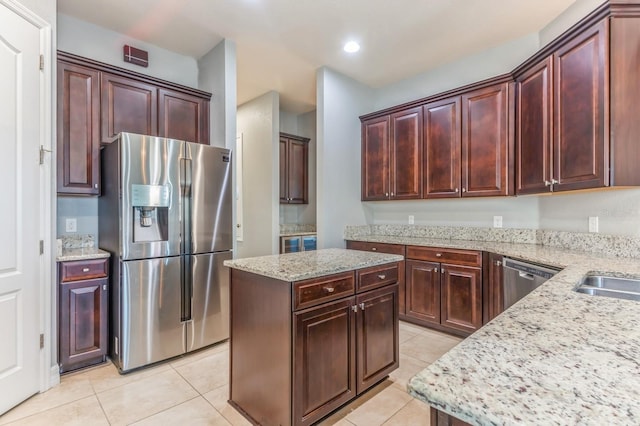 kitchen featuring appliances with stainless steel finishes, light tile patterned flooring, a center island, and light stone counters