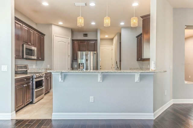 kitchen with a kitchen breakfast bar, kitchen peninsula, hanging light fixtures, light stone countertops, and appliances with stainless steel finishes