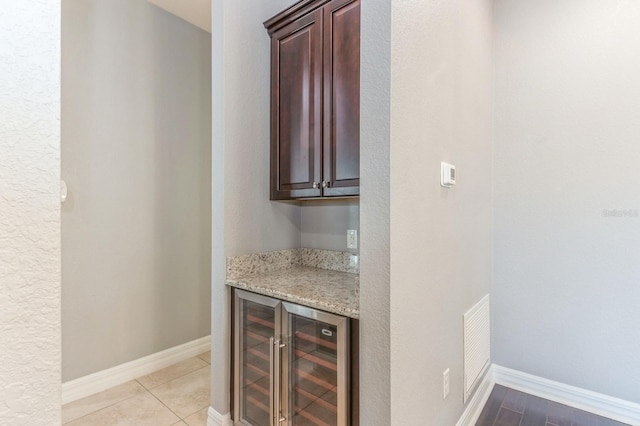 bar with light stone countertops, light tile patterned flooring, and wine cooler