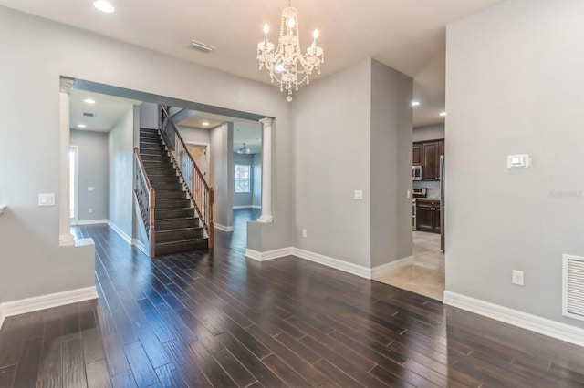 foyer entrance featuring decorative columns, a notable chandelier, and dark wood-type flooring