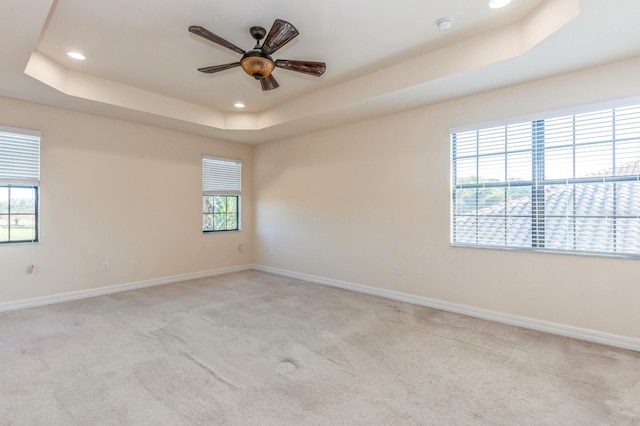 unfurnished room featuring ceiling fan, light colored carpet, and a raised ceiling