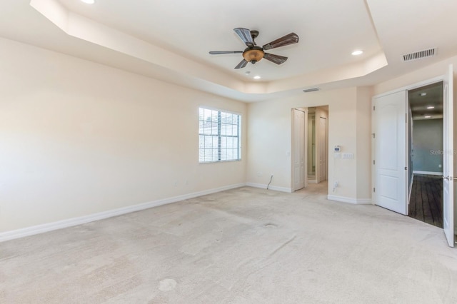 unfurnished bedroom with ceiling fan, a tray ceiling, and light colored carpet