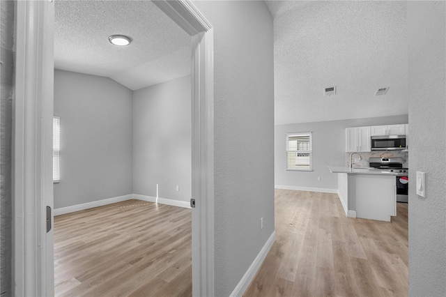 hall with light wood-type flooring, vaulted ceiling, a textured ceiling, and sink