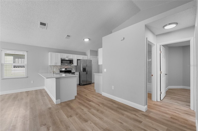 kitchen with kitchen peninsula, tasteful backsplash, light wood-type flooring, white cabinetry, and appliances with stainless steel finishes