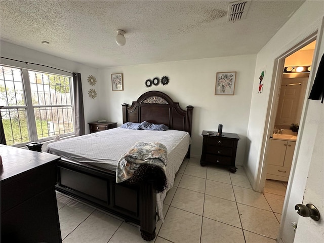 bedroom with a textured ceiling, connected bathroom, and light tile patterned flooring