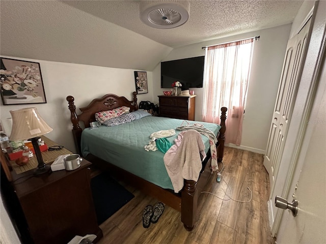 bedroom with a textured ceiling, vaulted ceiling, and wood-type flooring