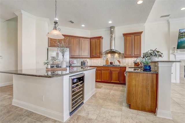 kitchen with built in refrigerator, a center island, wall chimney range hood, dark stone countertops, and wine cooler