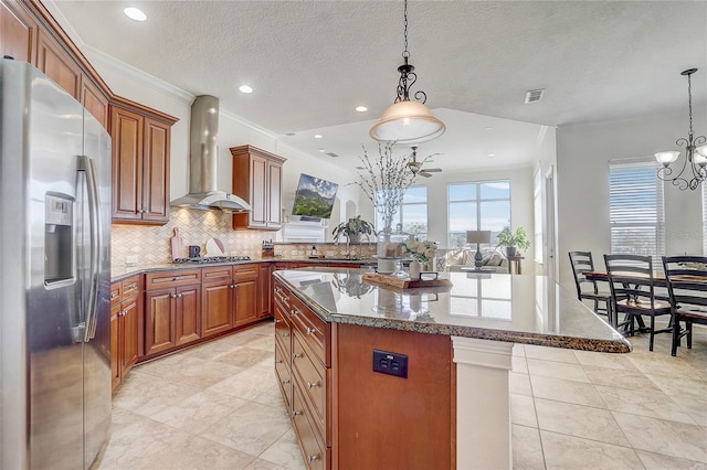 kitchen featuring appliances with stainless steel finishes, wall chimney exhaust hood, a kitchen island, decorative light fixtures, and crown molding