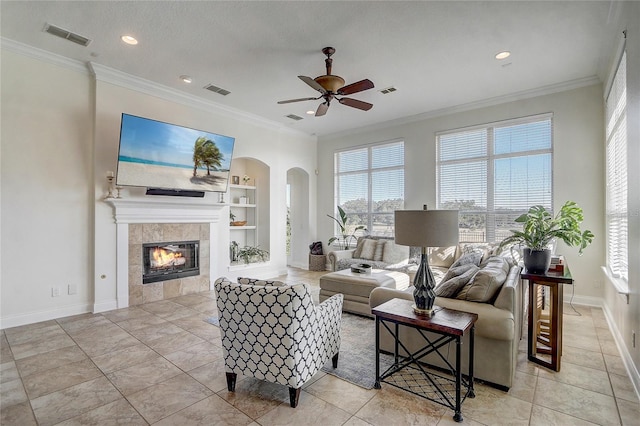 tiled living room featuring ceiling fan, crown molding, a fireplace, and built in shelves