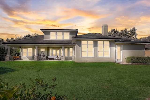 back house at dusk featuring a patio area, outdoor lounge area, and a yard