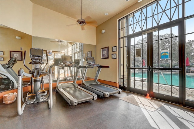 gym with a textured ceiling, ceiling fan, a towering ceiling, and french doors