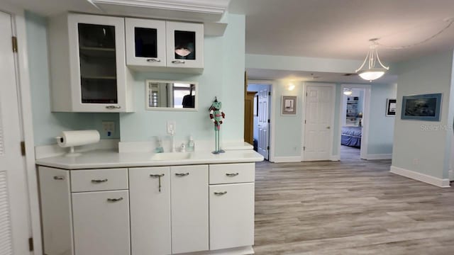 kitchen with white cabinetry, light hardwood / wood-style floors, hanging light fixtures, and sink