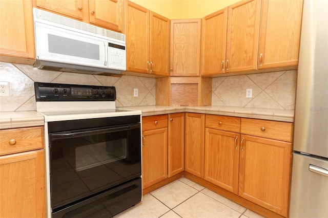 kitchen featuring tile counters, stainless steel fridge, light tile patterned floors, tasteful backsplash, and electric range