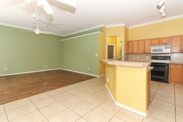 kitchen featuring electric range oven, ornamental molding, ceiling fan, an island with sink, and decorative backsplash