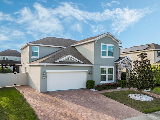 traditional home with a shingled roof, stone siding, decorative driveway, a gate, and stucco siding