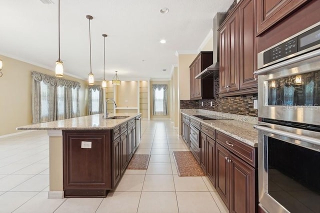 kitchen with double oven, sink, backsplash, hanging light fixtures, and a kitchen island with sink