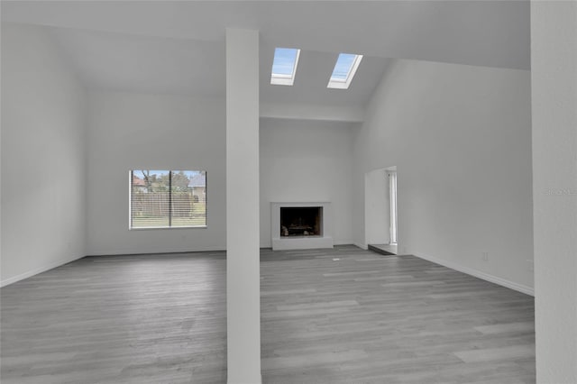 unfurnished living room with high vaulted ceiling, a skylight, and light hardwood / wood-style floors