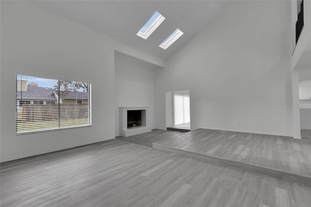 unfurnished living room with plenty of natural light, a skylight, a towering ceiling, and light wood-type flooring