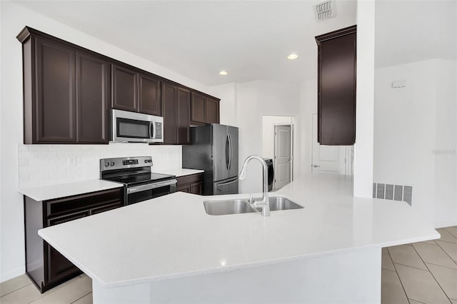 kitchen with kitchen peninsula, tasteful backsplash, appliances with stainless steel finishes, light tile patterned flooring, and sink