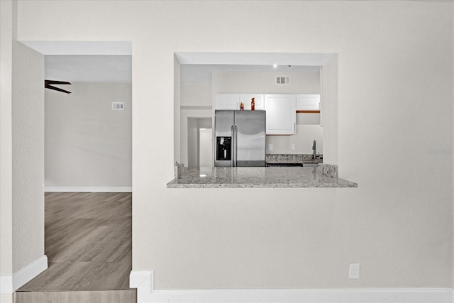 kitchen with ceiling fan, sink, white cabinets, stainless steel fridge, and light stone counters