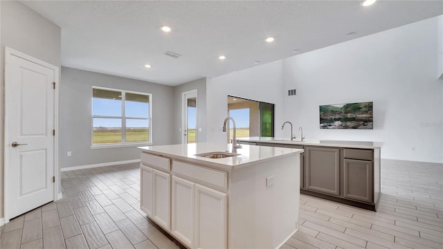 kitchen with an island with sink, white cabinets, sink, and a textured ceiling