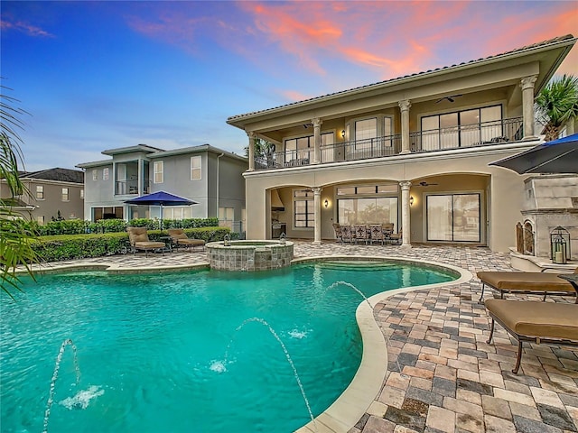 pool at dusk featuring pool water feature, ceiling fan, an in ground hot tub, and a patio