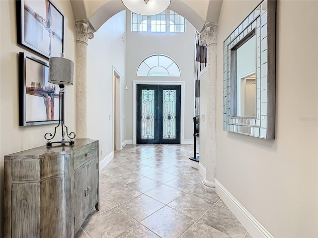 foyer entrance with a towering ceiling, french doors, a healthy amount of sunlight, and ornate columns