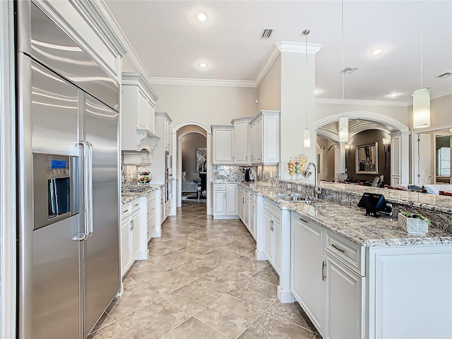 kitchen featuring hanging light fixtures, tasteful backsplash, white cabinets, stainless steel built in refrigerator, and sink