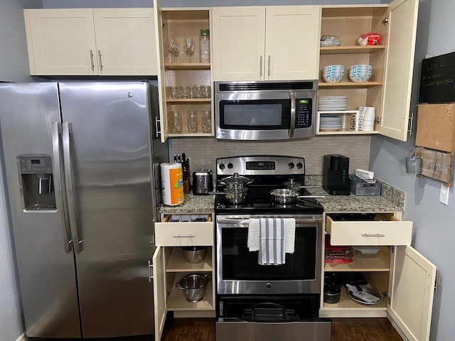 kitchen featuring stainless steel appliances, white cabinets, decorative backsplash, and dark stone counters