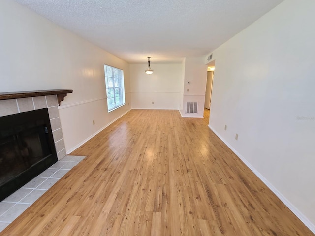 unfurnished living room featuring a textured ceiling, a tiled fireplace, and light hardwood / wood-style floors