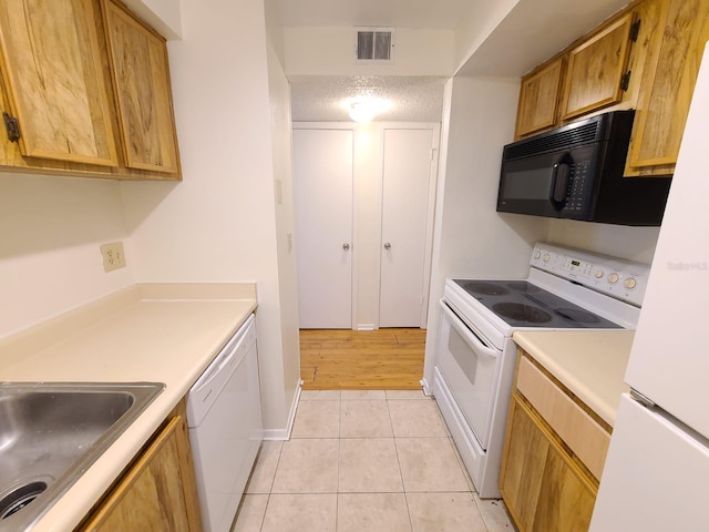 kitchen featuring sink, white appliances, a textured ceiling, and light tile patterned flooring