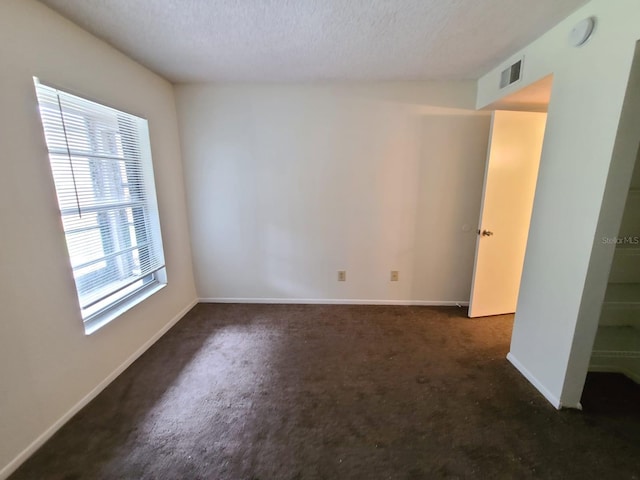 empty room with a textured ceiling and dark carpet