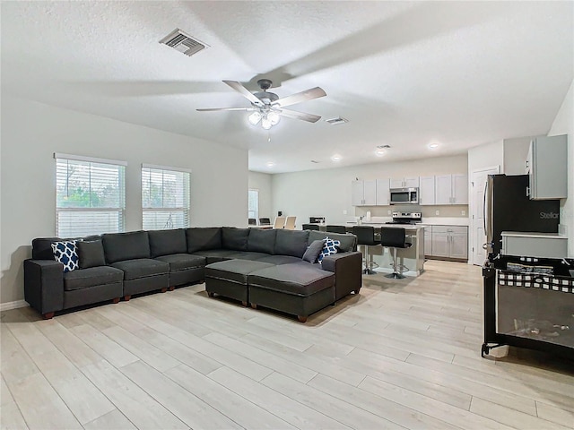 living room featuring ceiling fan, a textured ceiling, and light wood-type flooring