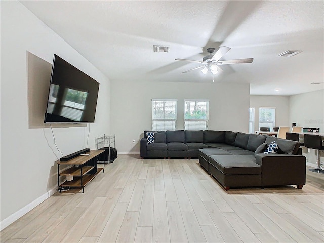 living room featuring ceiling fan, light hardwood / wood-style floors, and a textured ceiling