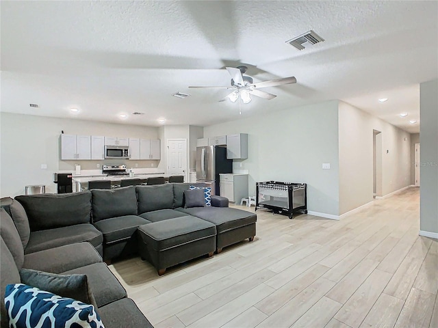 living room featuring ceiling fan, a textured ceiling, and light hardwood / wood-style floors