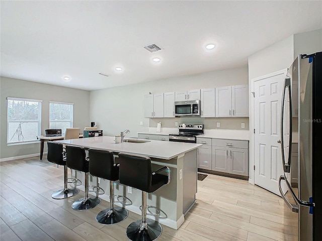 kitchen featuring sink, a kitchen breakfast bar, stainless steel appliances, a center island with sink, and light hardwood / wood-style flooring