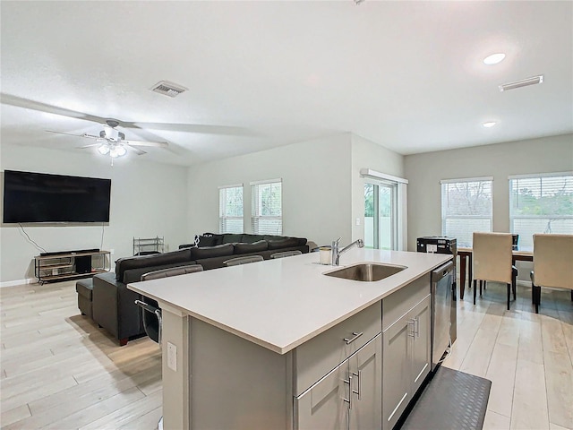 kitchen featuring dishwasher, sink, a center island with sink, and gray cabinetry