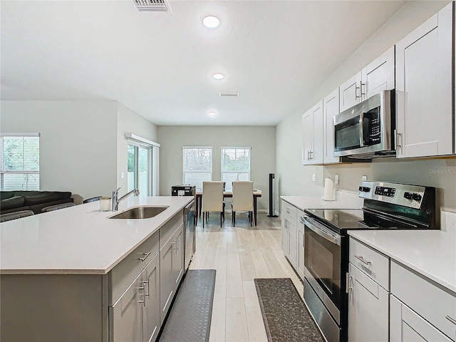 kitchen with sink, light hardwood / wood-style flooring, appliances with stainless steel finishes, a kitchen island with sink, and white cabinetry