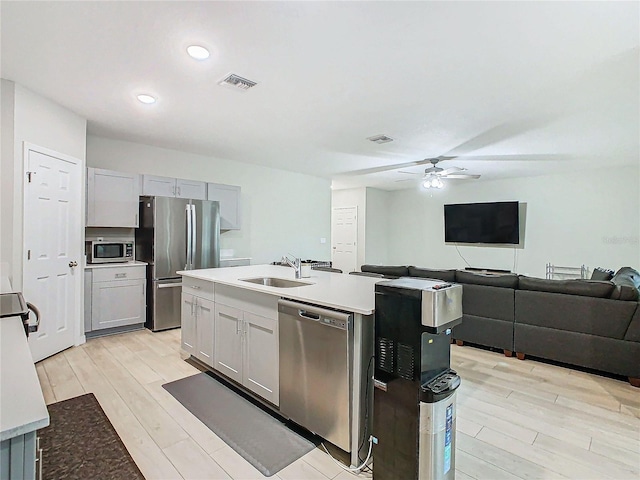 kitchen with sink, a kitchen island with sink, ceiling fan, stainless steel appliances, and light hardwood / wood-style flooring