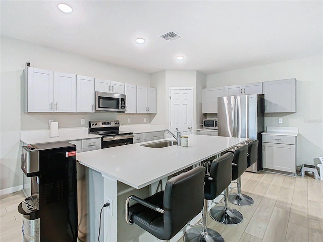 kitchen with sink, appliances with stainless steel finishes, light hardwood / wood-style floors, an island with sink, and a kitchen bar