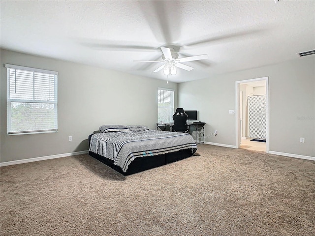 carpeted bedroom featuring ceiling fan, ensuite bath, multiple windows, and a textured ceiling