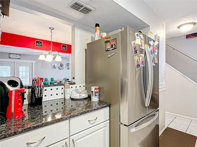 kitchen featuring an inviting chandelier, stainless steel fridge, decorative light fixtures, dark stone countertops, and white cabinets