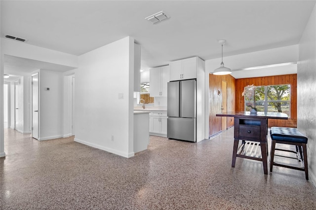 kitchen with pendant lighting, stainless steel fridge, sink, and white cabinets