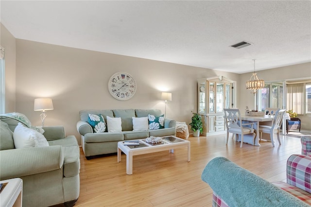 living room featuring light wood-type flooring, an inviting chandelier, and a textured ceiling