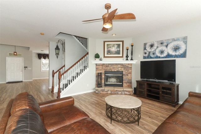 living room with ceiling fan, light hardwood / wood-style floors, and a stone fireplace