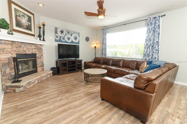 living room with ceiling fan, light hardwood / wood-style floors, and a stone fireplace