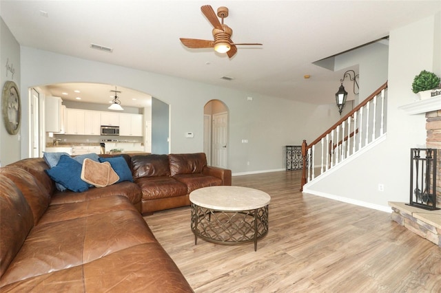 living room featuring a fireplace, ceiling fan, and light wood-type flooring